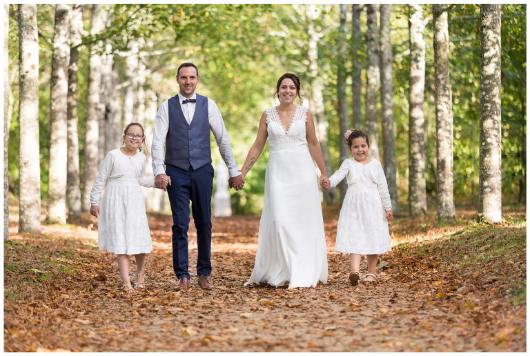 Les jeunes mariés et leurs enfants marchent de front d'un pas décidé sur un tapis de feuilles mortes.
